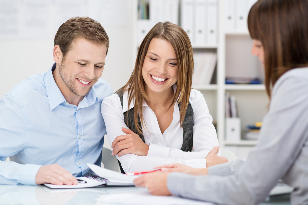 Investment adviser giving a presentation to a friendly smiling young couple seated at her desk in the office